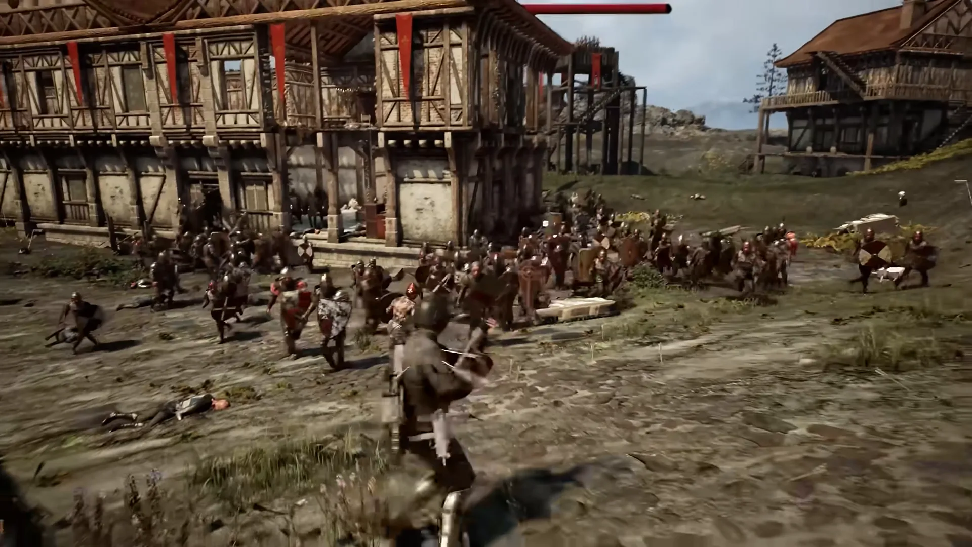 A dense crowd of soldiers with red tunics and shields charges through a village of timber-framed houses.