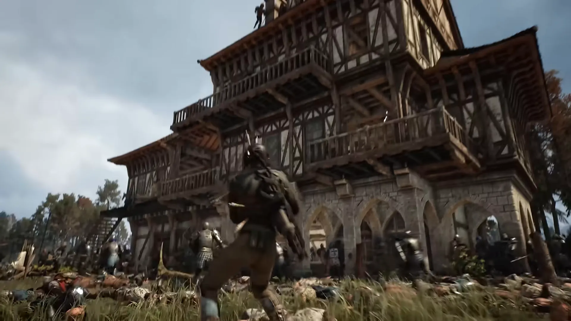 A soldier runs toward a very tall timber-framed building with balconies, bodies scattered on the grass in front.