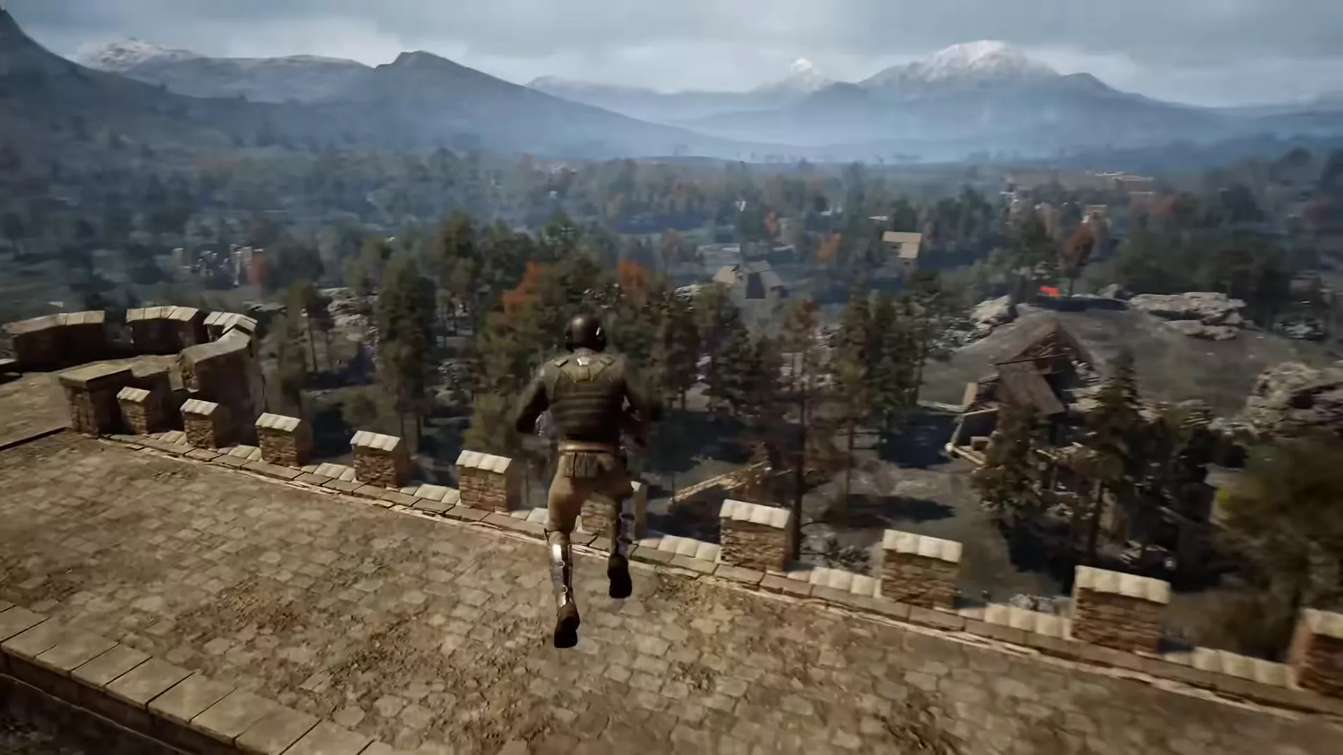 A soldier runs along a stone wall walkway with crenellations, above a town and wooded valley with mountains behind.